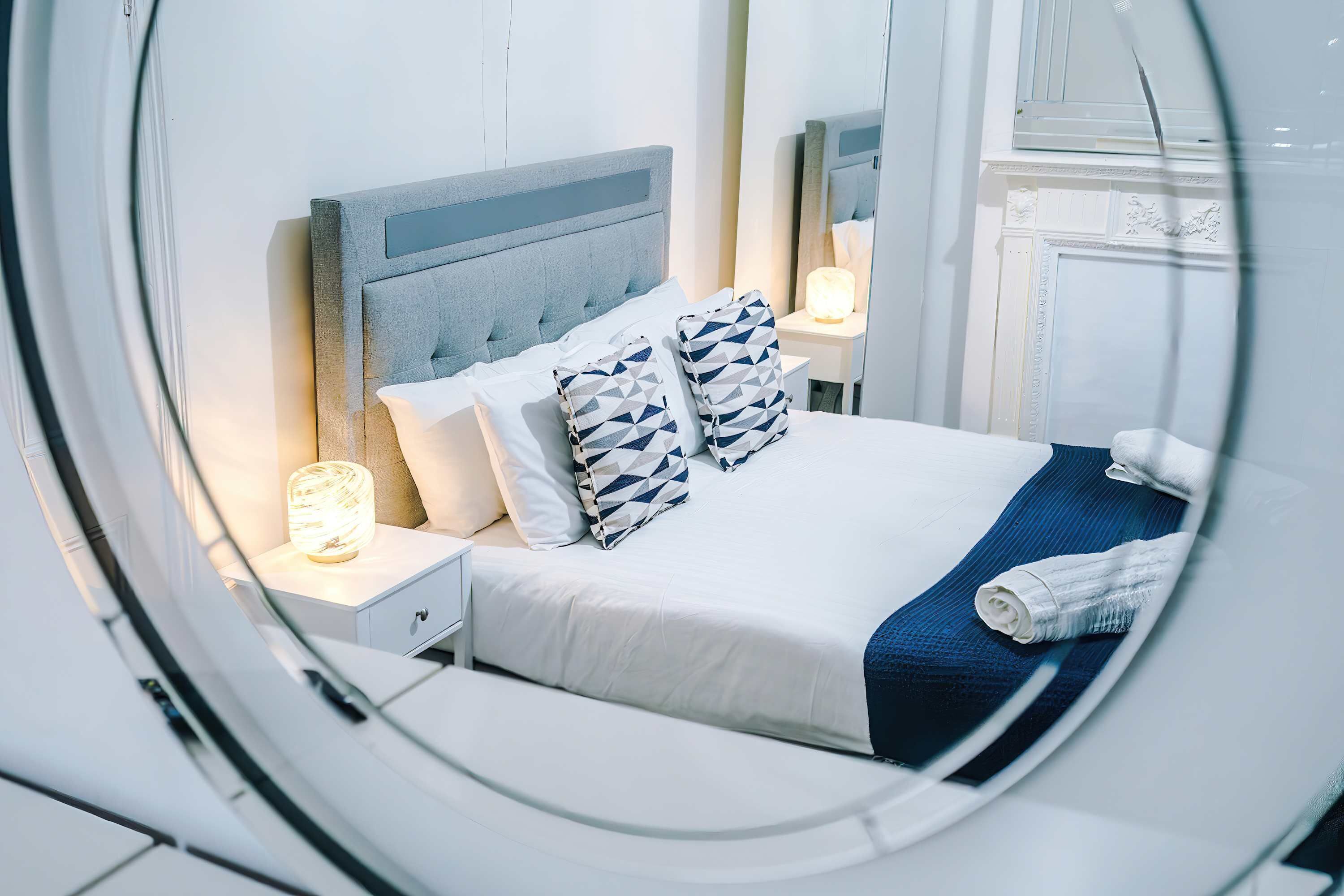 A hotel room with a bed, nightstands, a lamp, and a mirror.