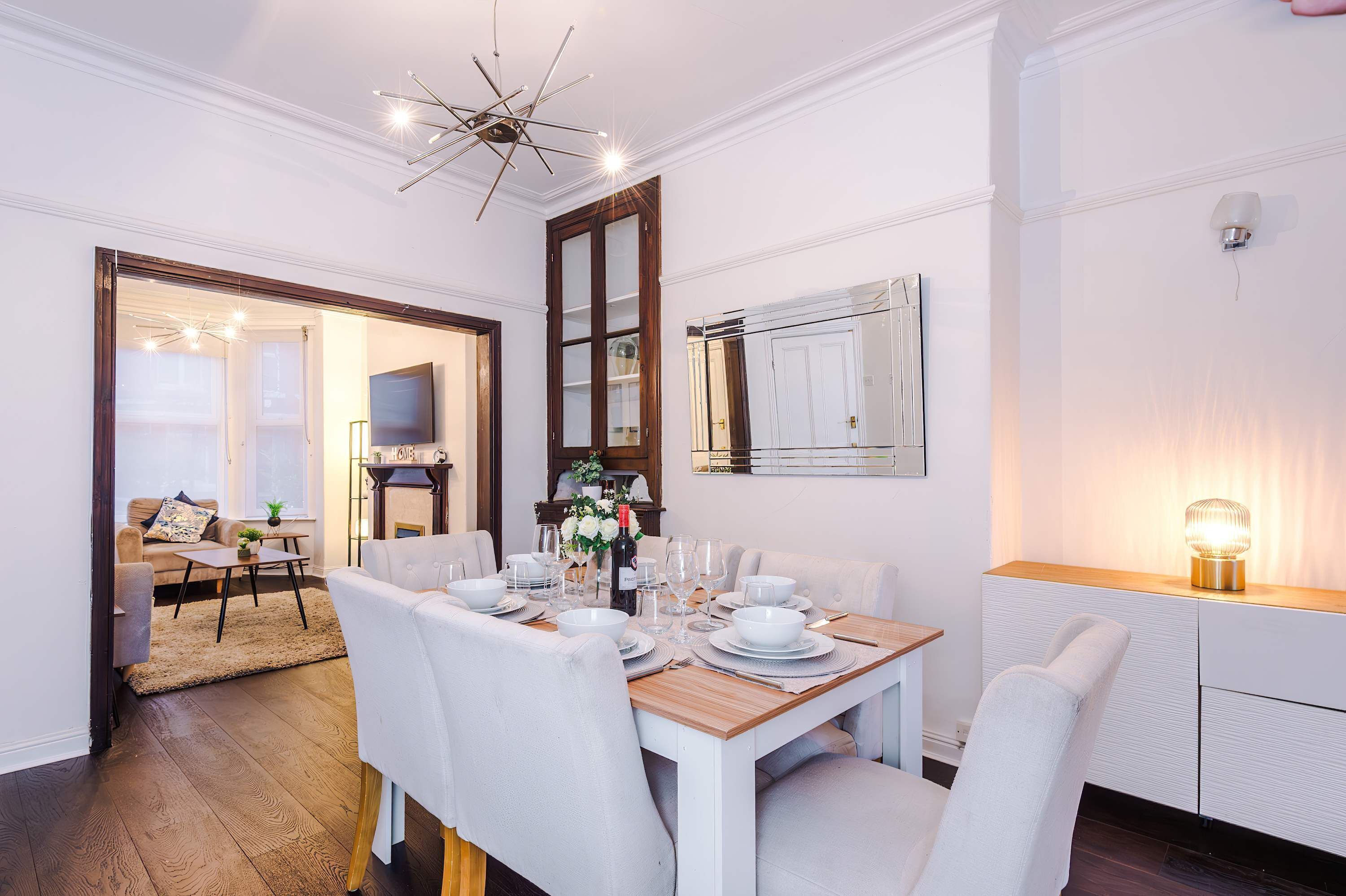 A dining area with a wooden table set for four, surrounded by white upholstered chairs.