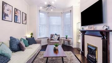 A living room with a sofa, coffee table, fireplace, and a TV mounted on the wall.