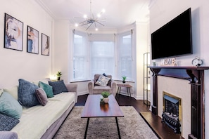 A living room with a sofa, coffee table, fireplace, and a TV mounted on the wall. - Bright 3BR Home Manchester Wi-fi Parking (Manchester)
