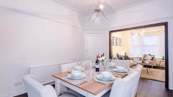 A dining area with a wooden table set for six, white chairs, and a modern chandelier.