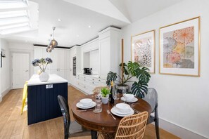 Cocina moderna con armarios blancos, una isla central y un comedor con mesa redonda para cuatro.