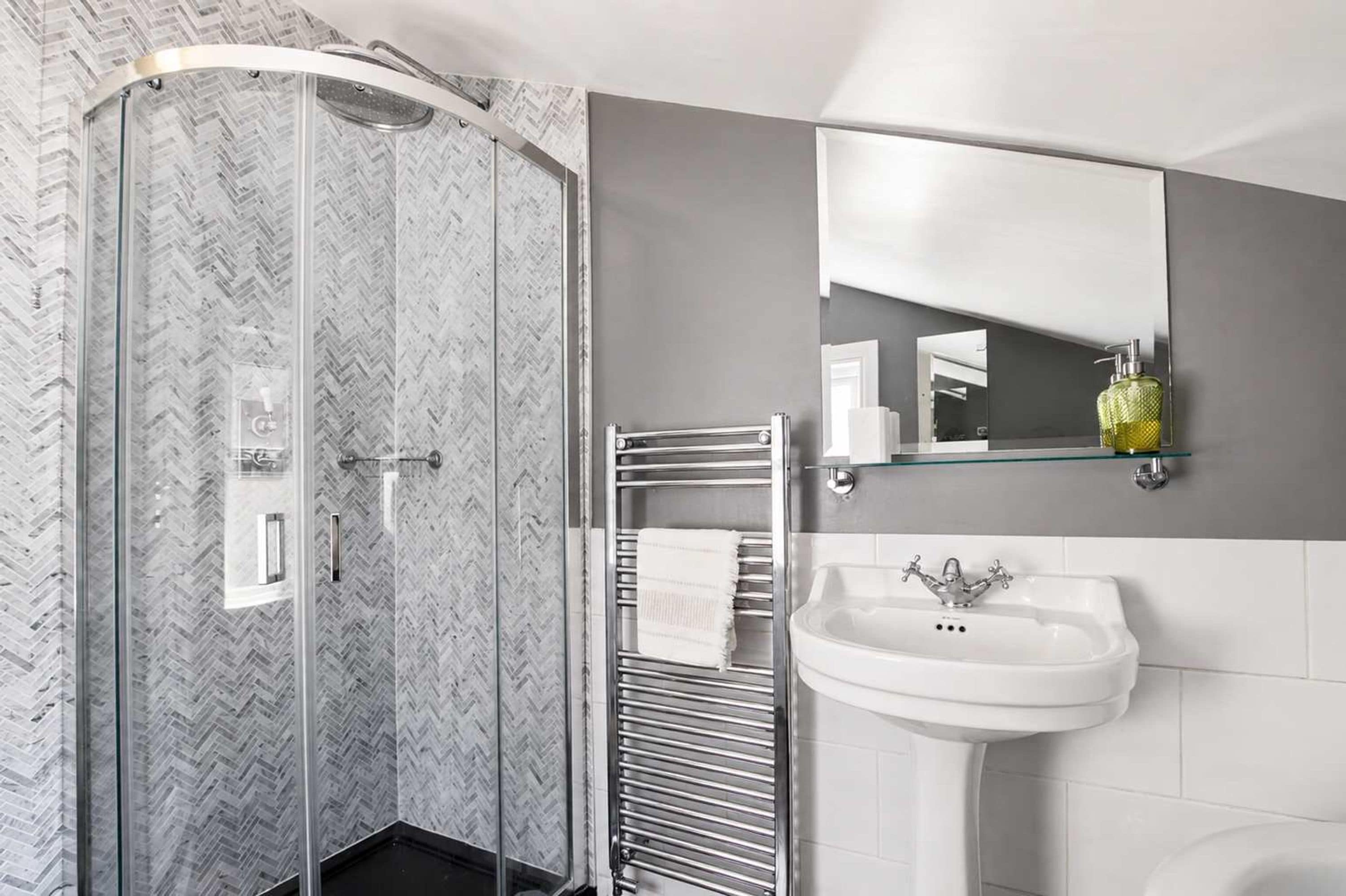 A modern bathroom with a glass-enclosed shower, a white sink, and a mirror above the sink.