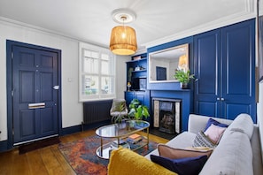 Una sala de estar con puerta azul, chimenea, sofá y lámpara colgante.