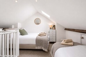 Un dormitorio moderno y luminoso en el ático, con techo inclinado, una cama con almohada verde, una mesita de noche con lámpara y un aparador con espejo.