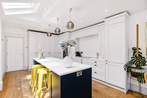 Una cocina moderna con armarios blancos, una isla central con taburetes, iluminación colgante y vistas al área de comedor contigua.