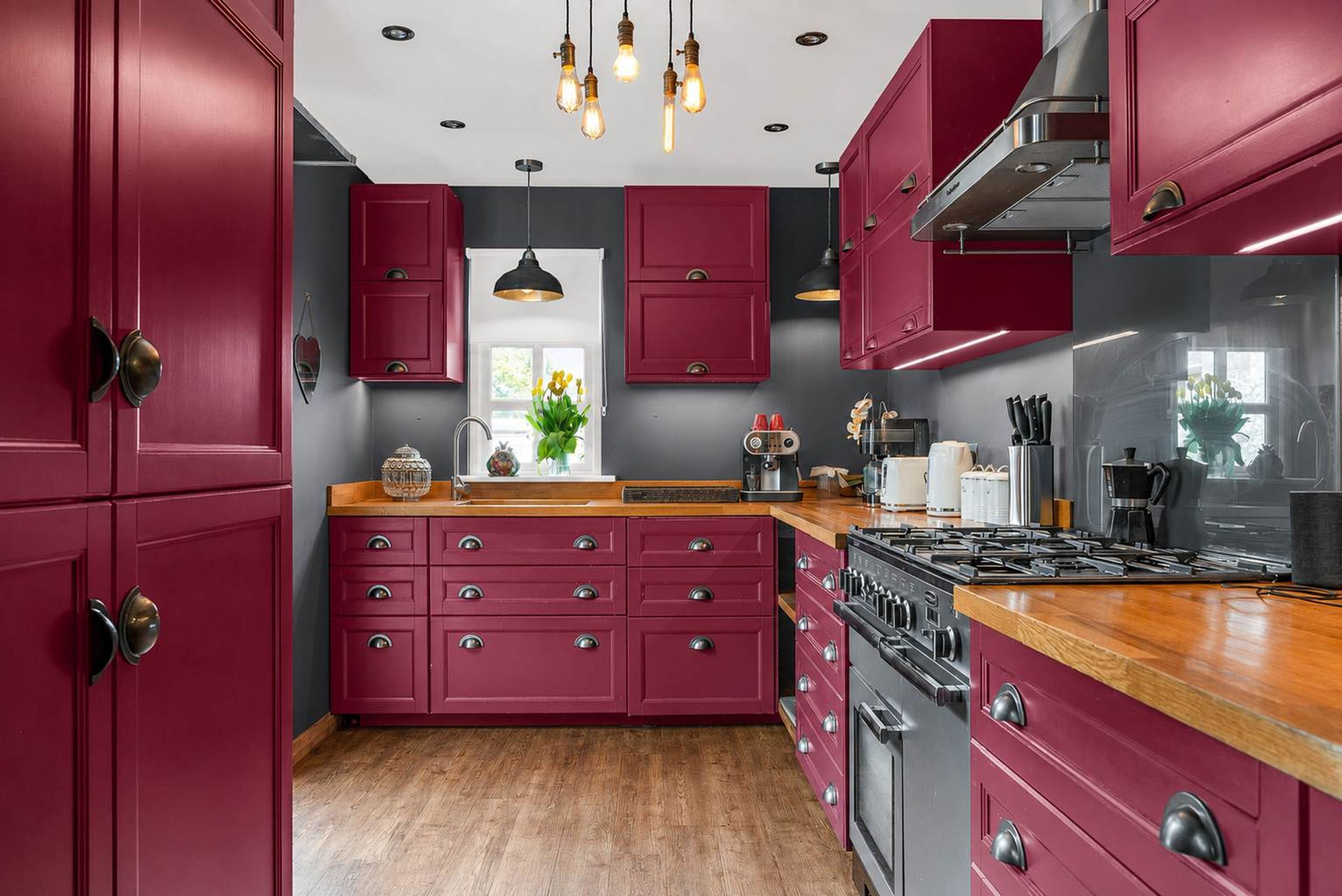 A kitchen with red cabinets, a wooden countertop, and a stove.