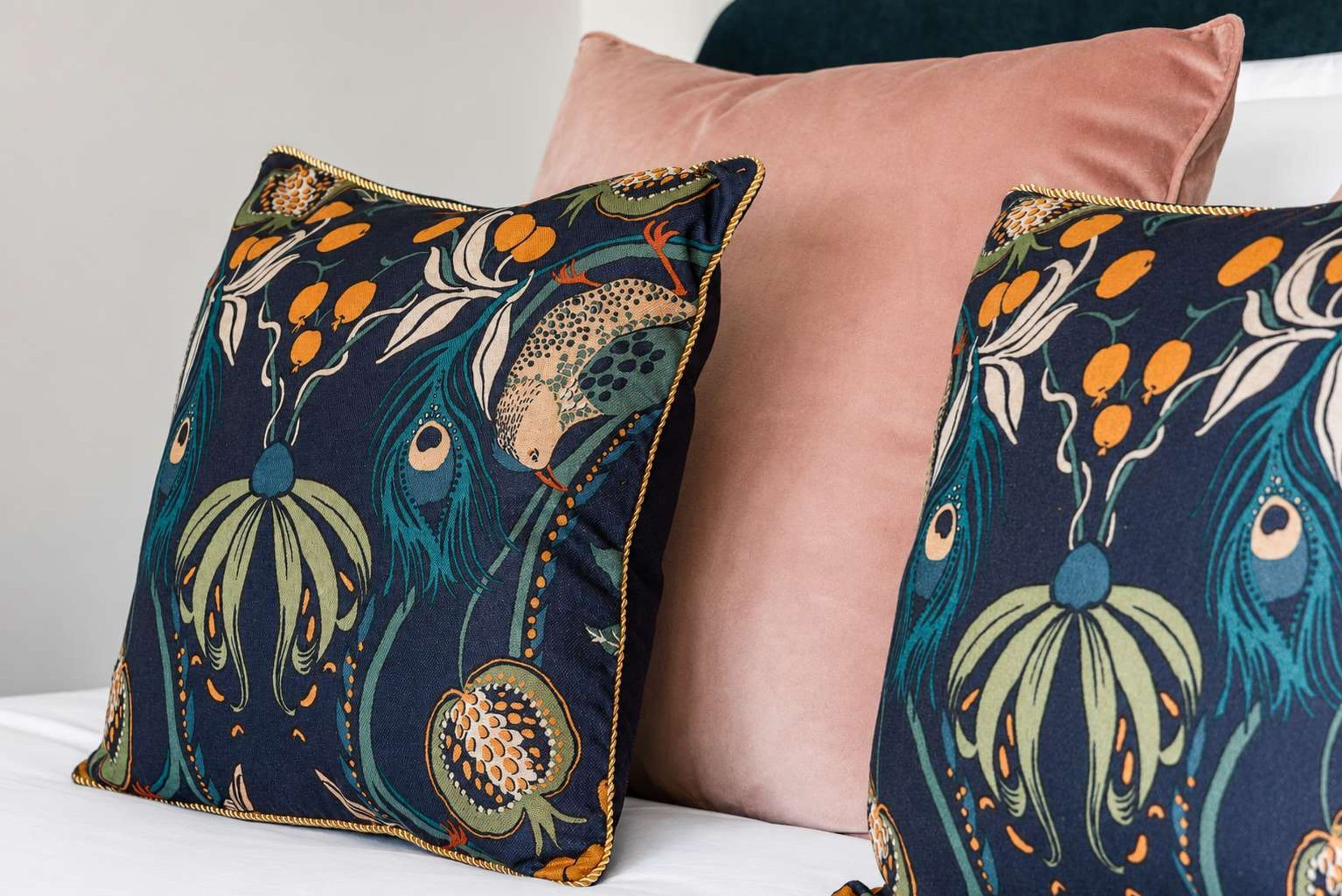 Deux coussins à motifs floraux orange et vert sur un fond bleu foncé, posés sur une surface blanche.