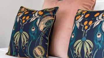 Deux coussins à motifs floraux orange et vert sur un fond bleu foncé, posés sur une surface blanche.