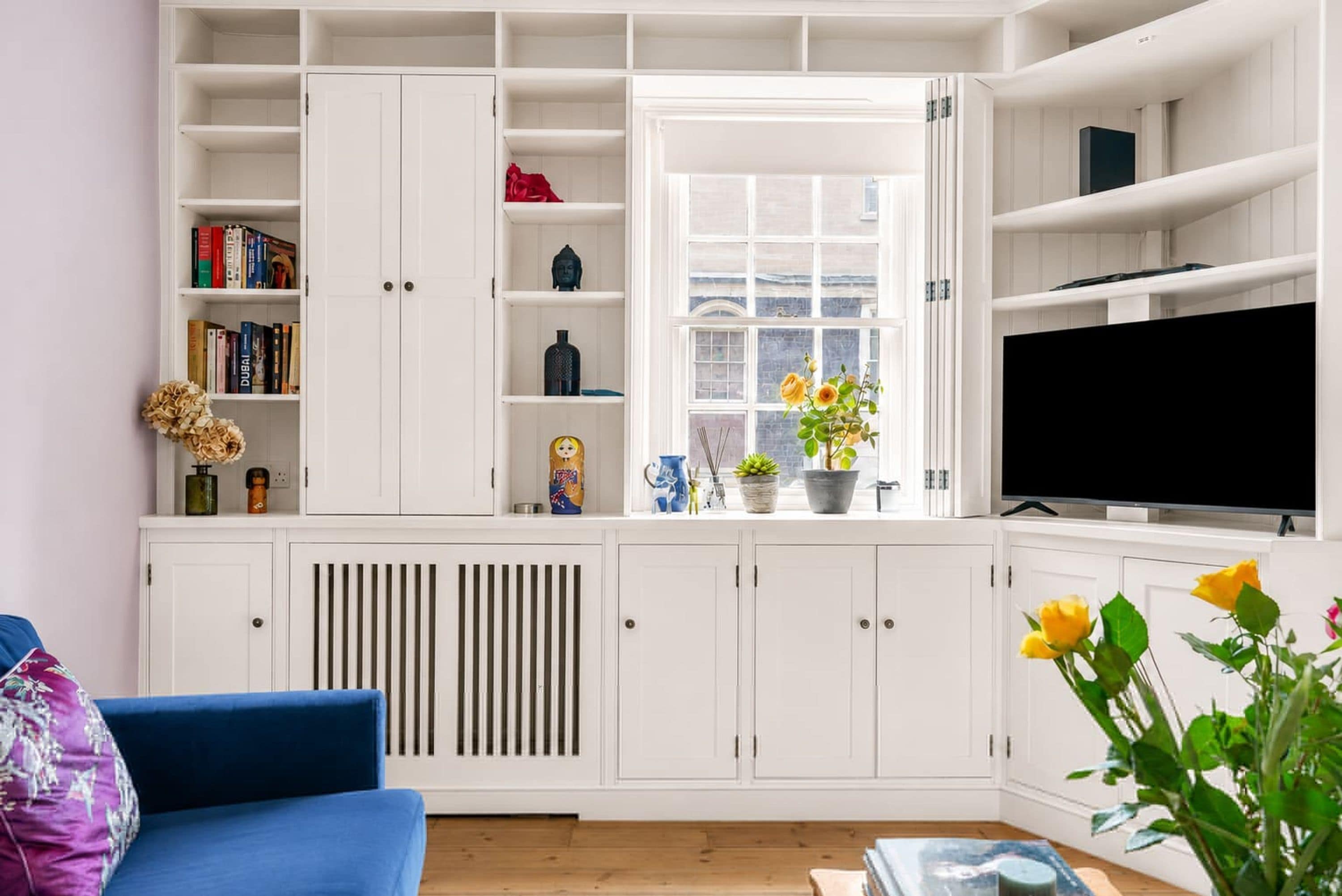 A modern living room with white cabinetry, a blue sofa, and a television.