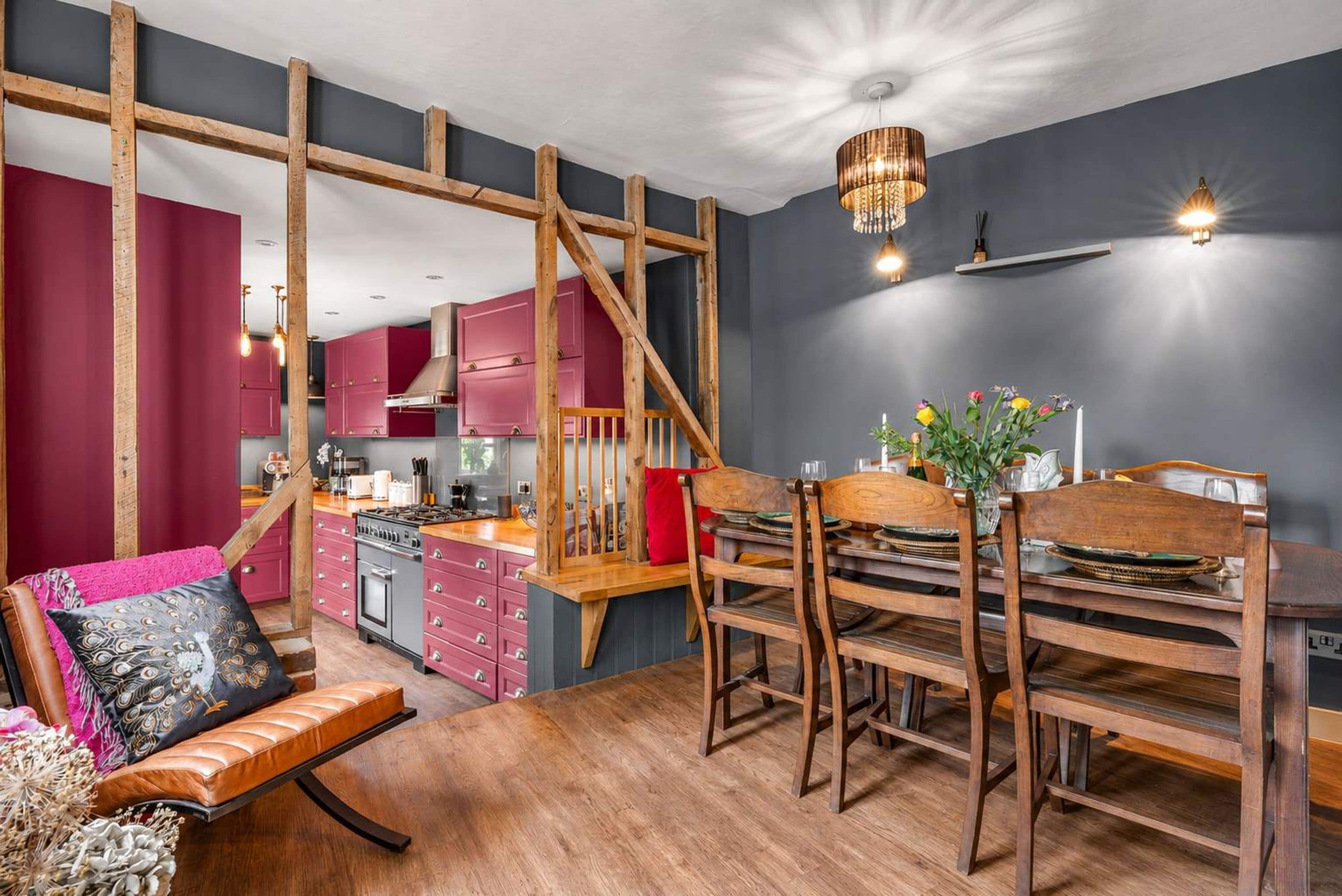 Una cocina moderna con vigas de madera, un comedor con mesa y sillas de madera, y una escalera.