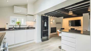 Una cocina moderna con armarios blancos, un refrigerador negro y una zona de comedor con televisor.
