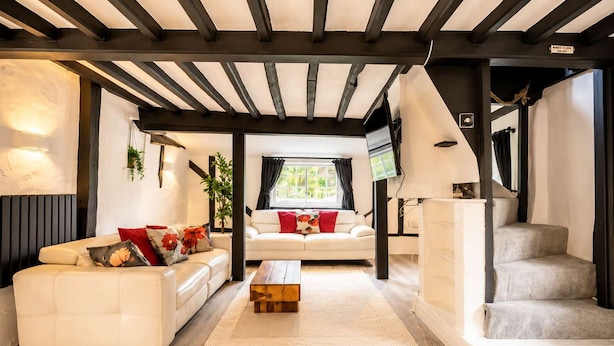 Sala de estar moderna com sofá branco, mesa de centro de madeira e escada para um andar superior.