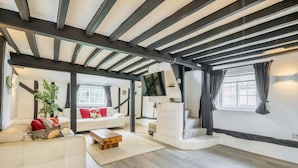Ampla sala de estar com pé direito alto, sofá branco, mesa de centro de madeira e uma grande janela com cortinas.