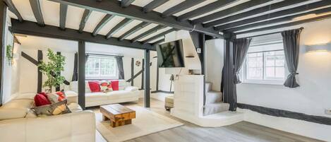 Un salón amplio con techo alto, un conjunto de sofá blanco, una mesa de centro de madera y un ventanal con cortinas.