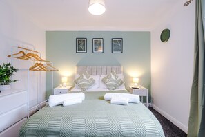 Ein ordentlich eingerichtetes Schlafzimmer mit Bett, Nachttischen, einer Kleiderstange und Wandbildern.