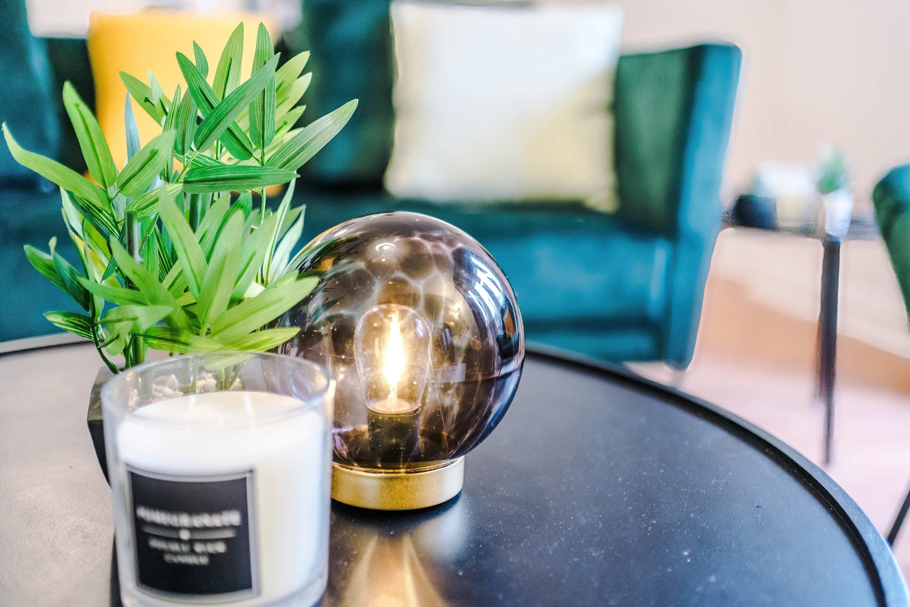 A round table with a glass candle holder, a lit candle, and a green plant.