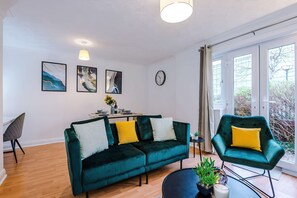 A modern living room with a green sofa, a dining table with chairs, and artwork on the walls. - 1BR Mediacity Flat Free Parking Near Lowry (Salford)