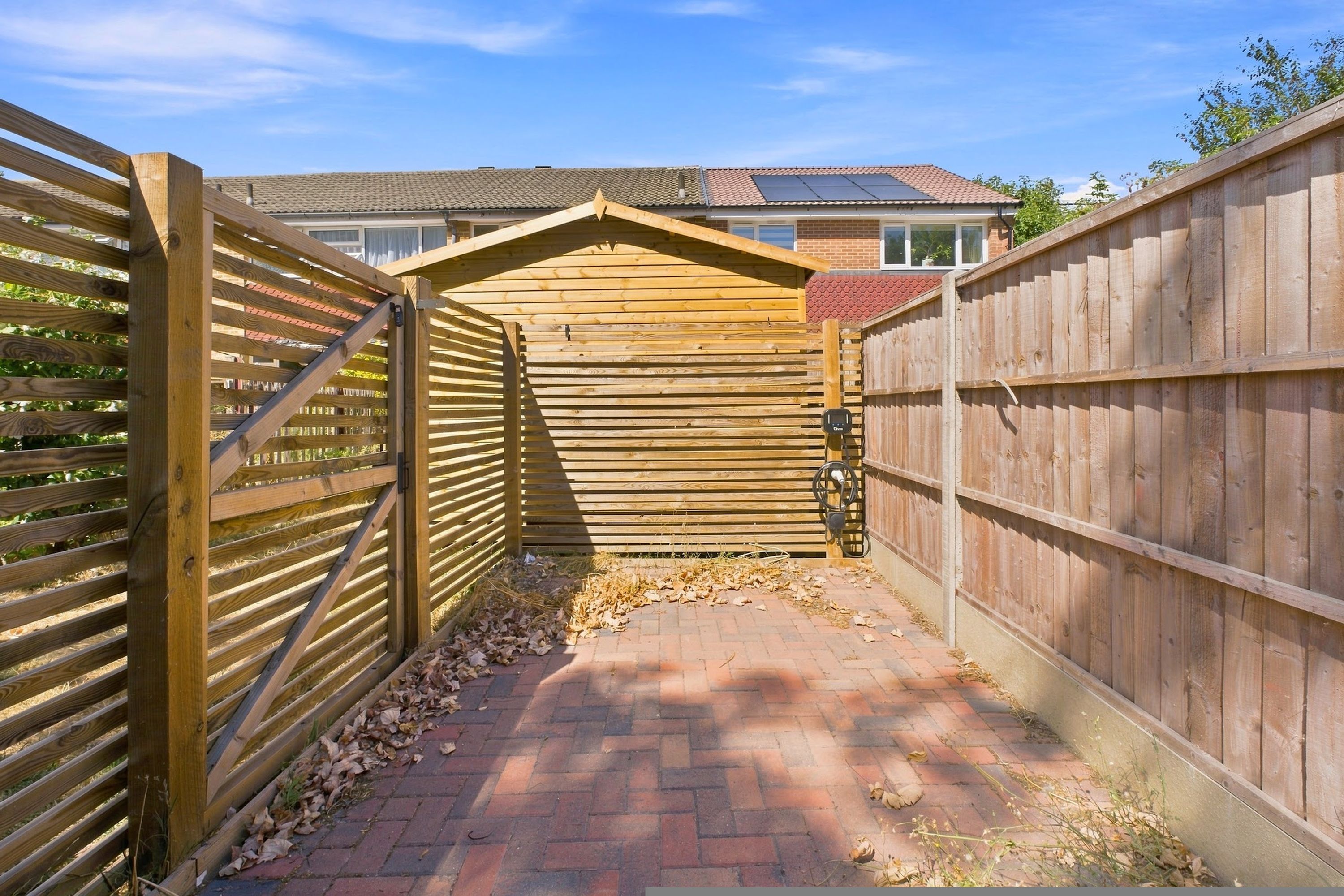 A wooden gate leading to a brick pathway with a house in the background.