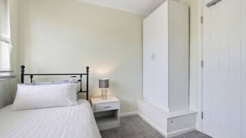 A bedroom with a bed, nightstand, lamp, wardrobe, and a door.