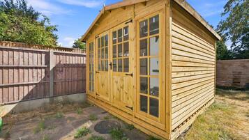 A wooden shed with a door and windows, a concrete pathway, and a wooden fence in the background.