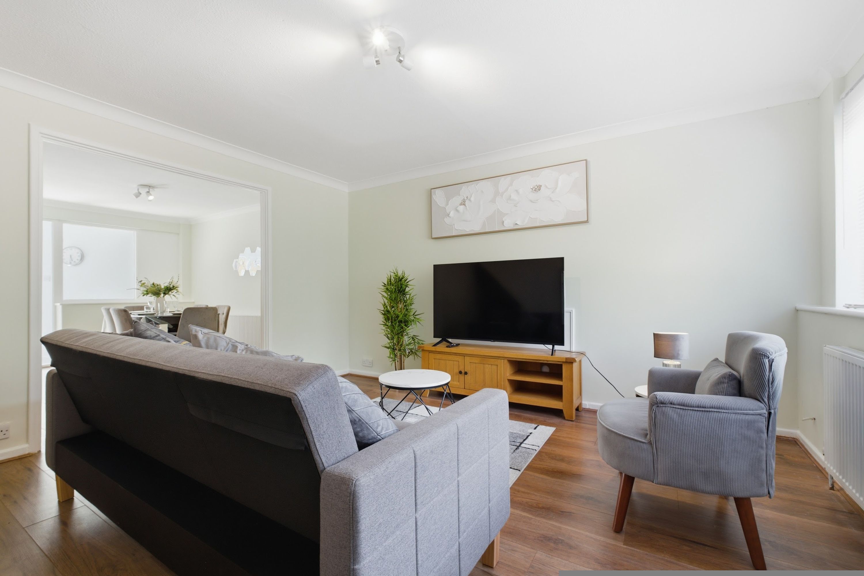 A modern living room with a grey sofa, a television on a wooden stand, a small round table, and a potted plant.