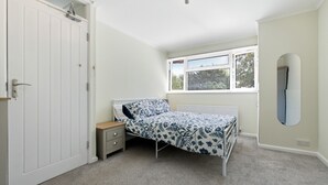 Ein Schlafzimmer mit einem Einzelbett, einem Nachttisch, einem Fenster mit Jalousien und einer Tür.