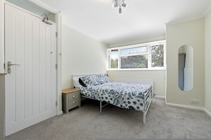 A bedroom with a single bed, a nightstand, a window with blinds, and a door. - Spacious 3-bed House in Waltham Cross Sleeps 6 (Waltham Cross)