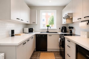 A modern kitchen with white cabinets, a built-in microwave, a dishwasher, and a stove. - Prime 3BR City Flat Balcony Walk to Shops (Manchester)