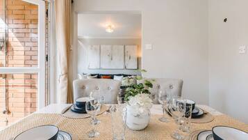 Un comedor con una mesa preparada para dos, un sofá al fondo y vistas a una pared de ladrillo y una puerta.