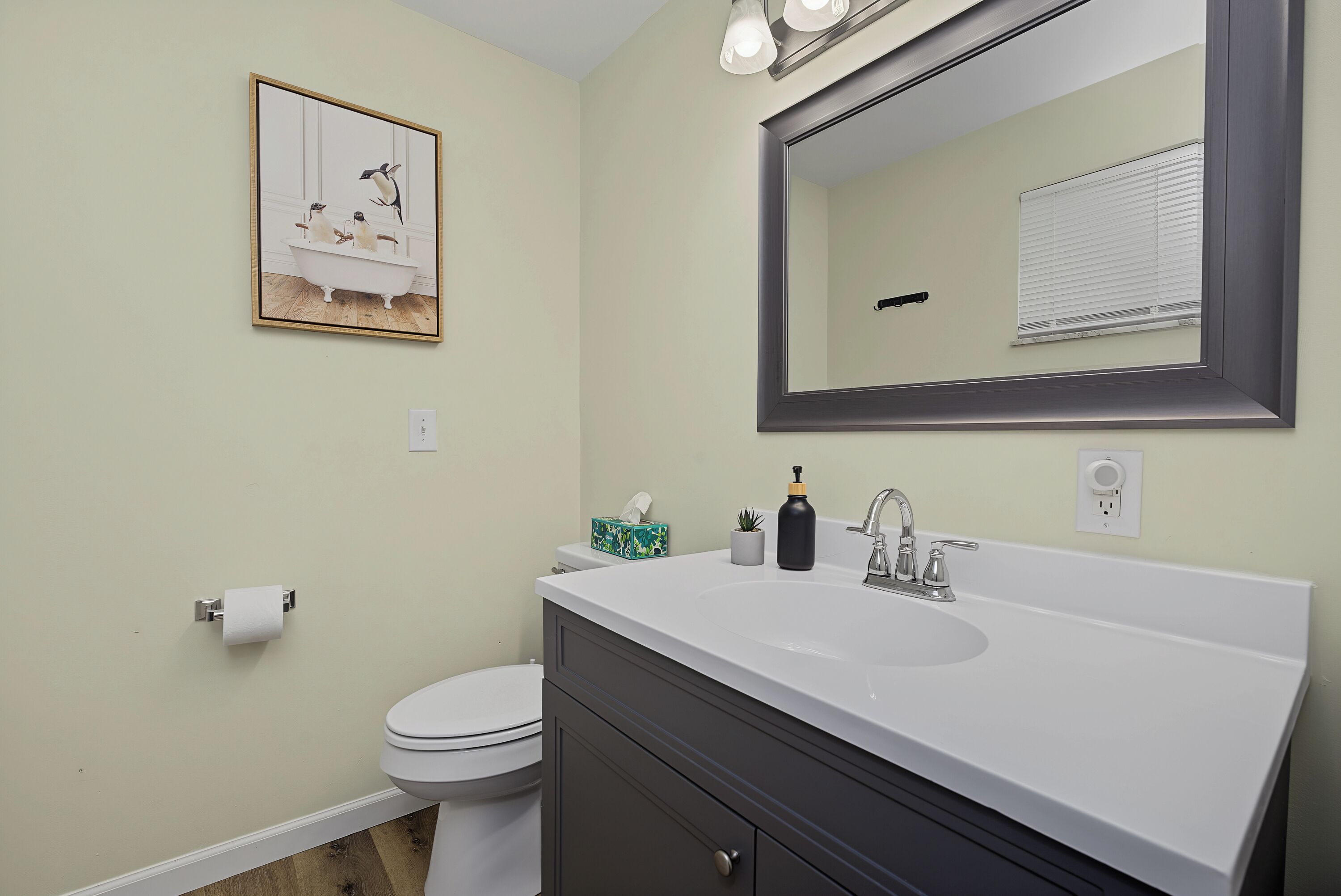 A bathroom with a white sink, a toilet, a mirror, and a framed picture on the wall.