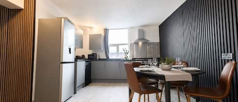 A modern kitchen with a dining area, featuring a refrigerator, microwave, and cabinets.