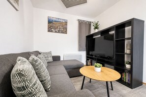 A modern living room with a grey sofa, a round wooden coffee table, a black entertainment unit with a TV, and a painting on the wall. - 2 Bed Manchester Free Parking Sleeps 4 (Manchester)