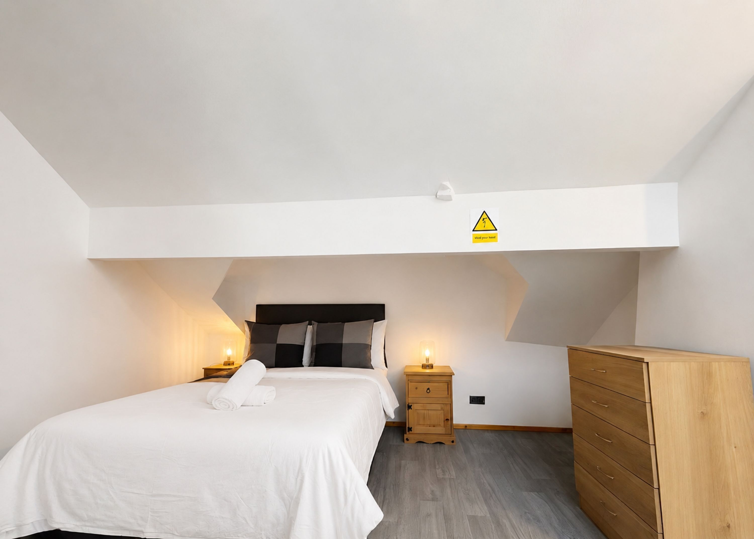 A bedroom with a bed, bedside tables, a dresser, and a warning sign on the ceiling.