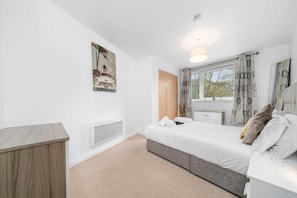 A modern bedroom with a bed, bedside tables, a radiator, and a window with curtains. - Sleek 2BR Edinburgh Near Murrayfield Sleeps 4 (Edinburgh)