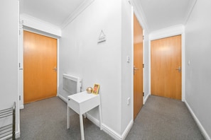 A hallway with two wooden doors, a white desk with a small decorative item, and a white wall with a welcome sign.