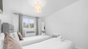 A hotel room with two single beds, a window with curtains, a bedside table, a chair, a flat-screen TV, and a ceiling light fixture. - Sleek 2BR Edinburgh Near Murrayfield Sleeps 4 (Edinburgh)