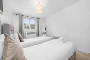 A hotel room with two single beds, a window with curtains, a bedside table, a chair, a flat-screen TV, and a ceiling light fixture. - Sleek 2BR Edinburgh Near Murrayfield Sleeps 4 (Edinburgh)