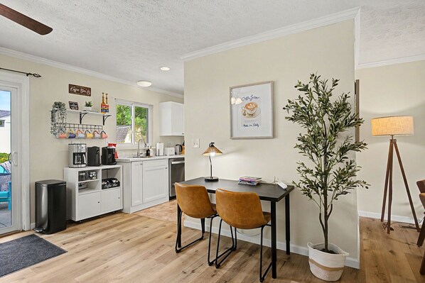 A compact kitchen with modern appliances, a dining area with two chairs, and a potted plant.