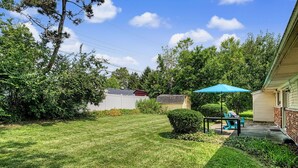 A backyard with a lawn, a patio with a table and chairs, and a small shed.