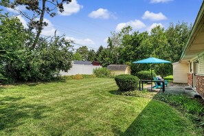 A backyard with a lawn, a patio with a table and chairs, and a small shed.