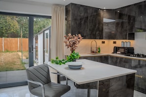 A modern kitchen with a white countertop, dark marble backsplash, and a dining area with a table and chair.