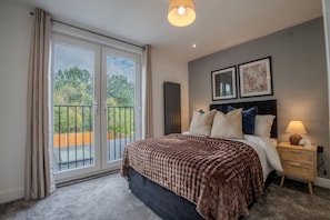 A bedroom with a large bed, a nightstand, a lamp, and a view of the outdoors through a sliding door.