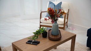 A wooden coffee table with a vase of flowers, a remote control, and a small potted plant. - Spacious 5bed House in Ruislip Sleeps 10 (Ruislip)