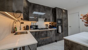 A modern kitchen with dark cabinetry, a built-in oven, and a microwave. - Spacious 5bed House in Ruislip Sleeps 10 (Ruislip)