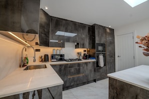 A modern kitchen with dark cabinetry, a built-in oven, and a microwave. - Spacious 5bed House in Ruislip Sleeps 10 (Ruislip)
