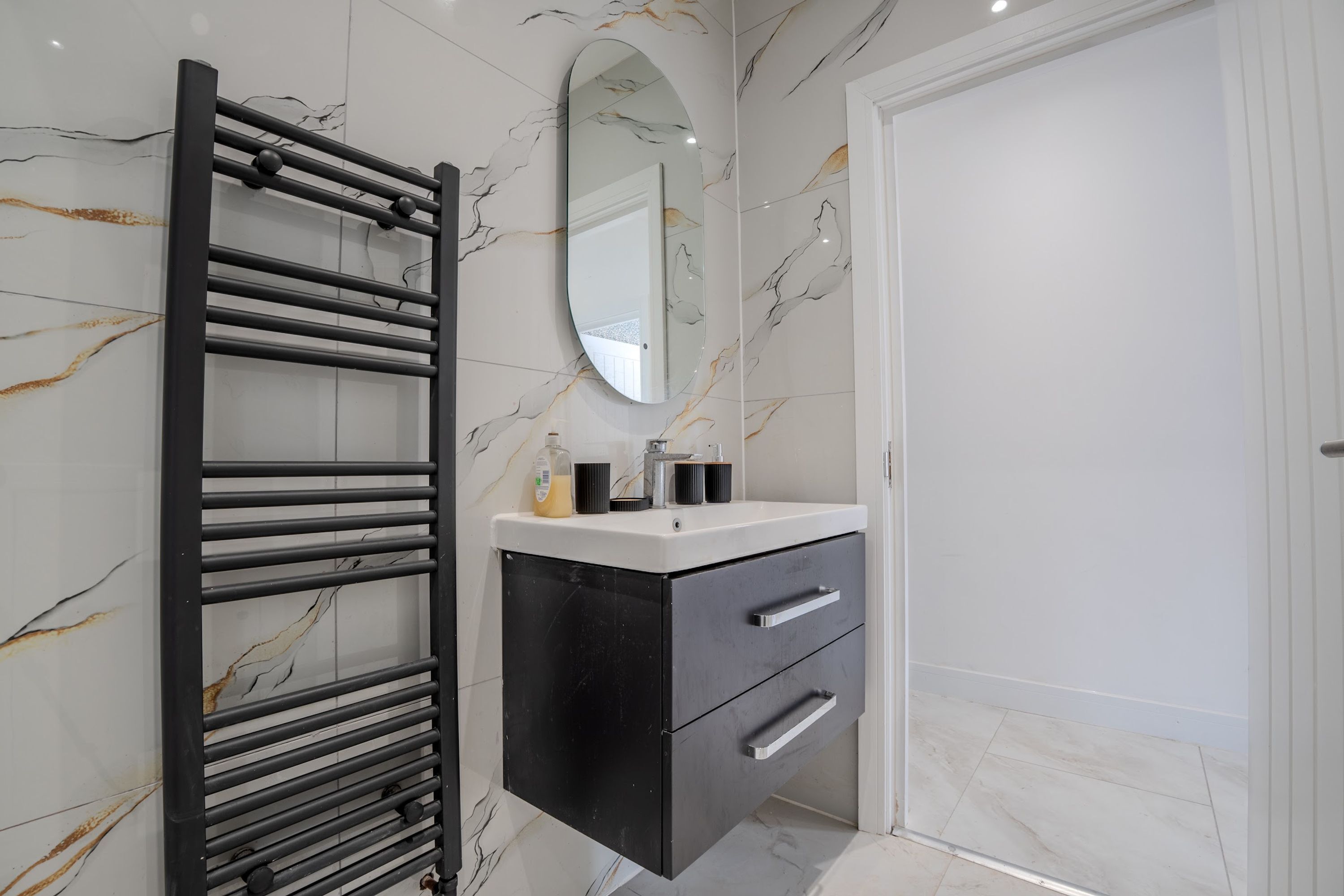 A bathroom with a black towel rack, a mirror, a white sink, and a black cabinet.