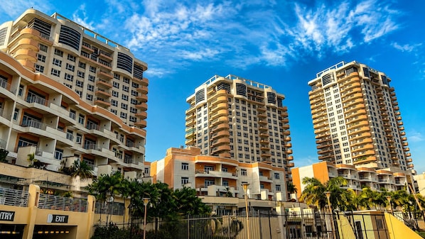Een hoog appartementencomplex met meerdere balkons, een heldere lucht en palmbomen op de voorgrond.