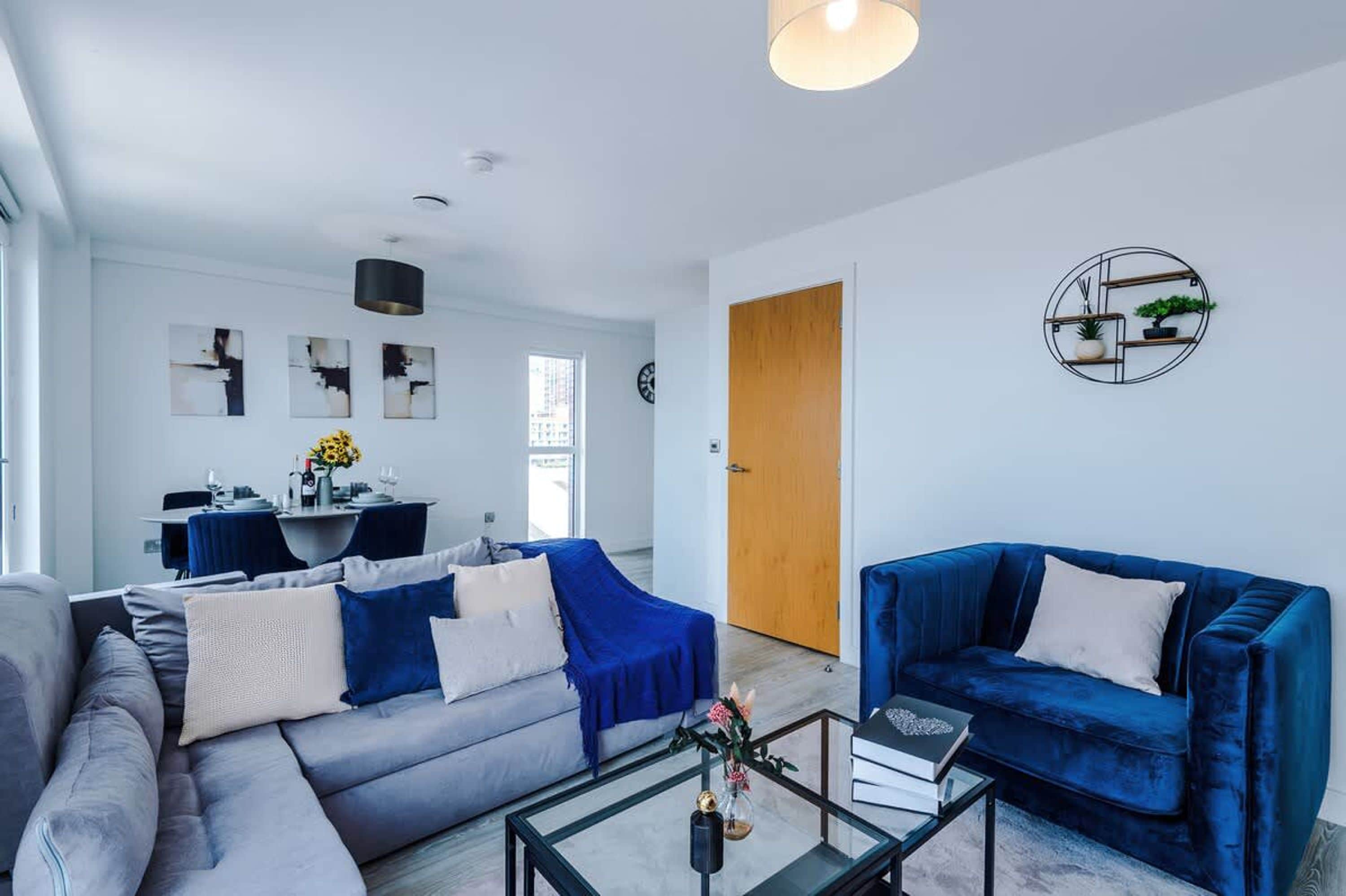 A modern living room with a sofa, a blue armchair, and a glass coffee table.