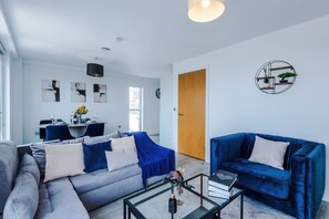 Een moderne woonkamer met een bank, een blauwe fauteuil en een glazen salontafel.